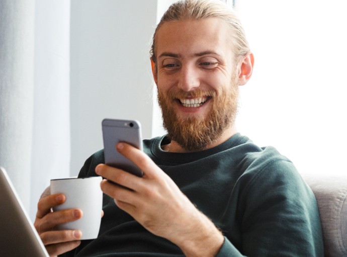 Man smiling at his phone while holding a mug
