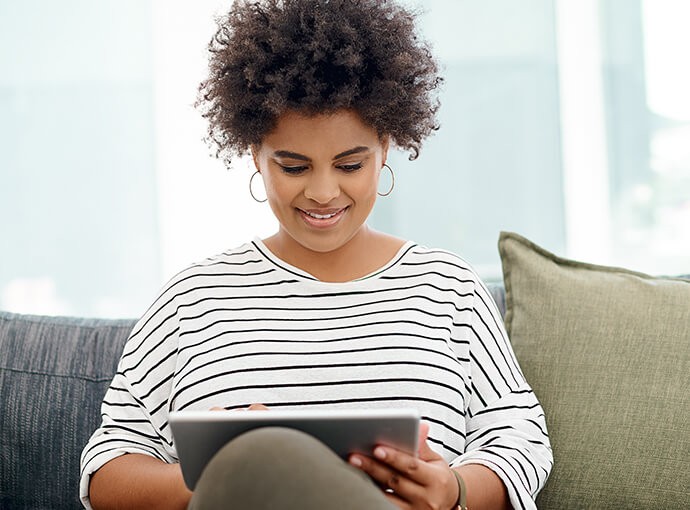 Woman sitting on couch looking at tablet.